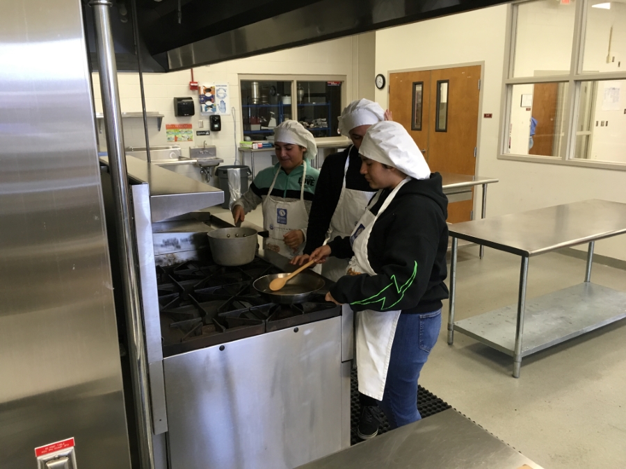 Students cooking food on a stove top.